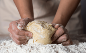 hands kneading dough on a floured surface